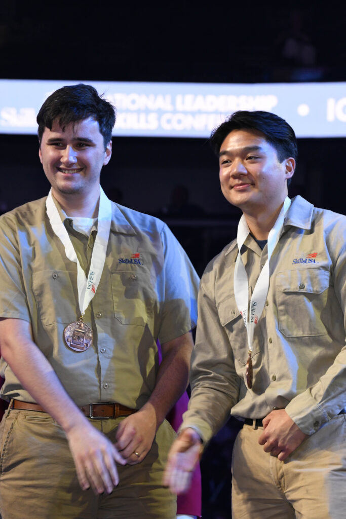 James Sutherland and Evan Chow on stage at NLSC 2025 with medals around their necks.